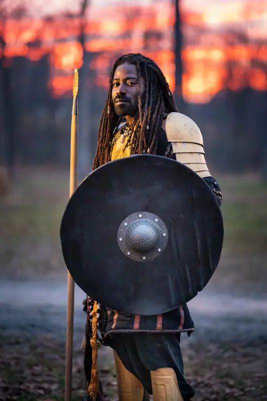 A club member in armor holding a round shield at dusk